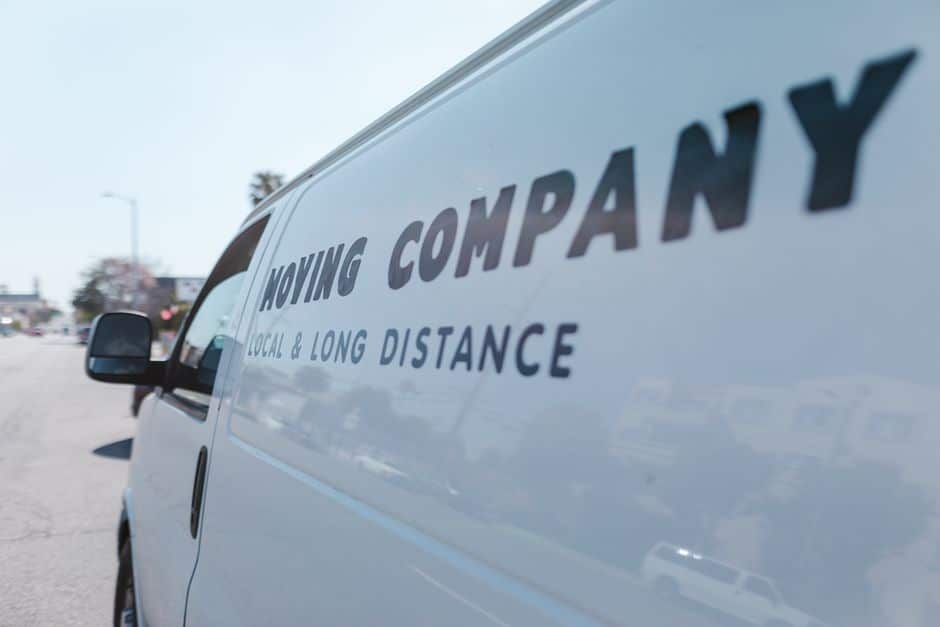 pexels-photo-7464677 - EZ Movers | New Orleans Moving Company White moving company van with the words 'MOVING COMPANY' and 'LOCAL & LONG DISTANCE' on the side, reflected in the window, parked on a street.