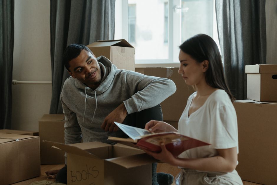 featured-4554377 - EZ Movers | New Orleans Moving Company Two people sit among moving boxes in a living room, one reading a magazine as they plan the move.